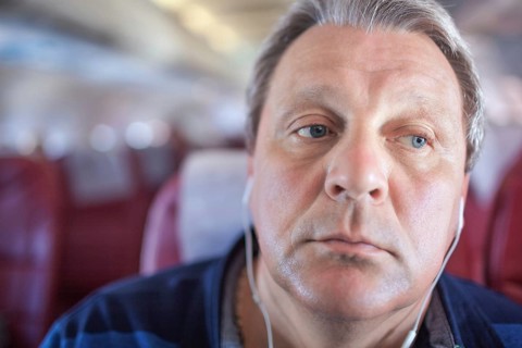 Close-up shot of mature man listening to music in headphones during traveling by plane. He looking