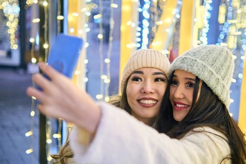 Two girlfriends asian girls in white coats are having fun hugging and selfie on mobile phone, new