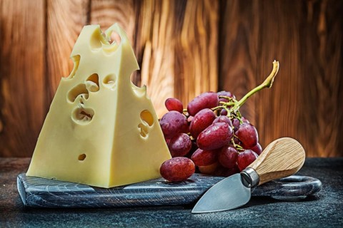 Piece of maasdam cheese on vintage carving board knife and bunch of rose grape old wooden