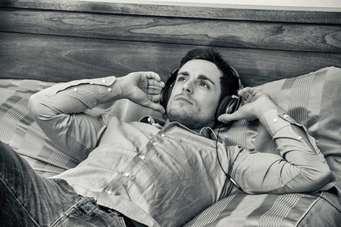 Handsome young man in bed listening to music with headphones, using cell phone or MP3 player