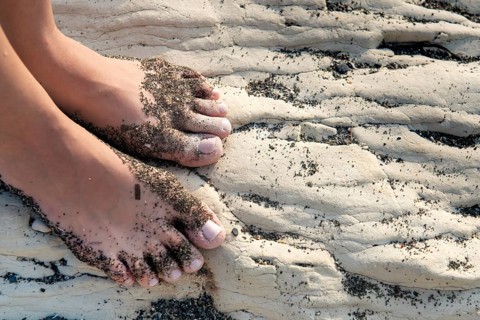 Unrecognised beautiful female food with beach sand on a white beach rocky surface