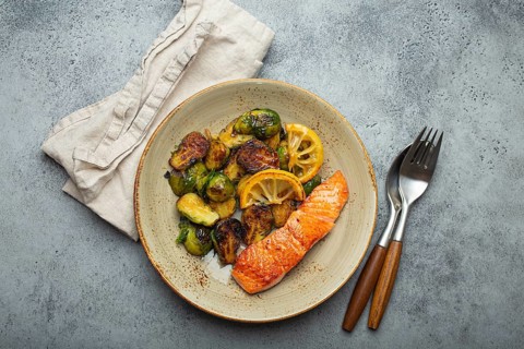 Delicious salmon fillet with grilled Brussels sprouts on plate, rustic stone background top view.