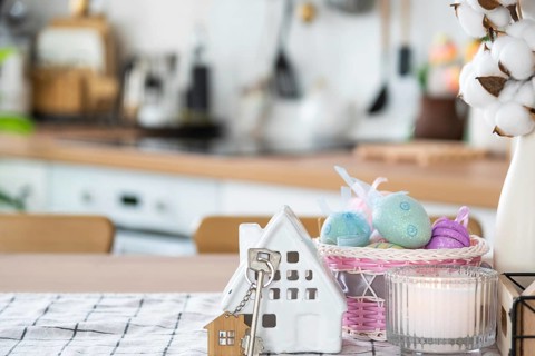Key and tiny house of cozy home with Easter decor with color eggs on table of kitchen. Building,