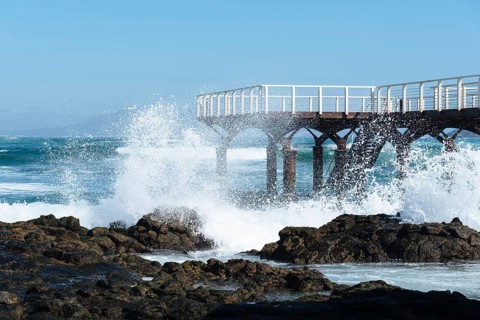 Waves breaking against pier on the beach of Corralejo at morning against blue sky
