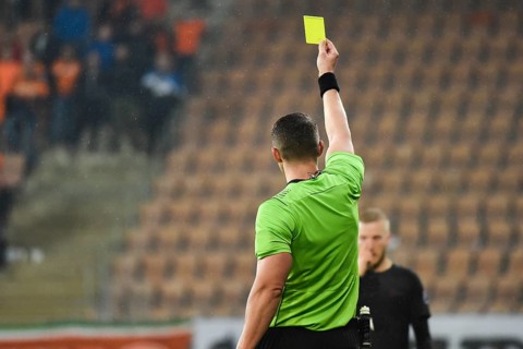 Referee shows footballer yellow card during soccer match at the stadium