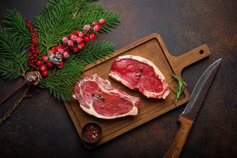 Two raw uncooked meat beef steaks on wooden cutting board with knife and seasonings on dark rustic
