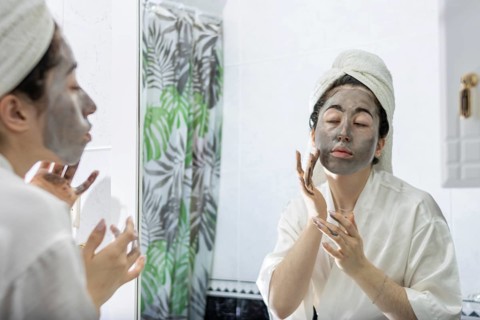 Portrait of a young woman applying a black cream face mask for skin in front of her bathroom mirror