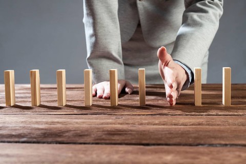 Businesswoman protecting dominoes from falling on wooden desk. Business assistance and leadership