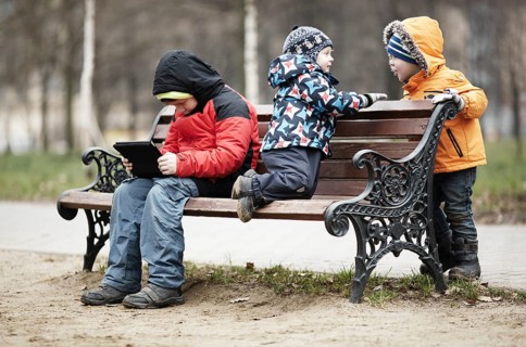 Three young boys playing on a park bench in winter wrapped up warmly against the cold weather with
