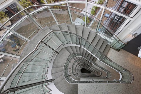 A modern spiral staircase with glass railings and a triangular shape in a bright room, Free and