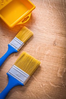 Two paintbrushes with blue handles and yellow paint can on wooden board construction concept