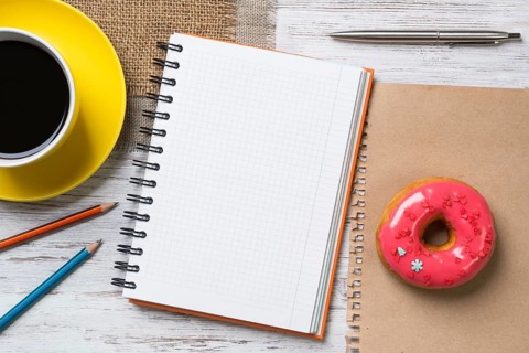 Opened notepad and cup of coffee with donut on wooden table