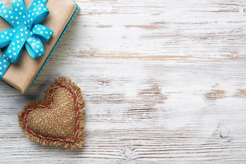 Flat lay cute composition with handmade fabric heart. Gift box with ribbon bow on wooden table.