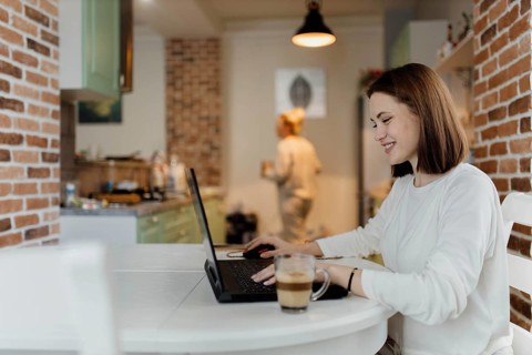 Woman happily using a laptop in a kitchen, enjoying her work with a relaxed demeanor