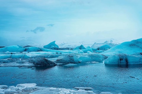Blue icebergs floating in a frigid body of water, surrounded by snowy mountains, iceberg Iceland,