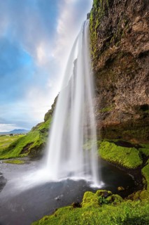 Sunny day in Iceland. Seljalandsfoss waterfall in July. Passage under the waterfall