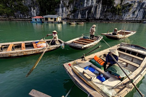Boats with people in front of a rock, during a calm river trip, rowing boats for tourists in Halong