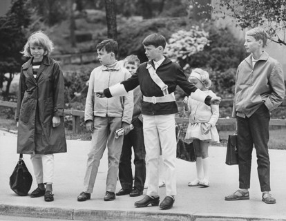 Junior safety patrol in the 1960s. A teenage boy stands with his arms out and signals to the