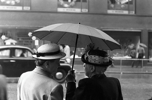 Umbrellas in the 1950s. The rain is pouring and two elderly ladies is seen holding an umbrella over