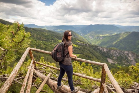 Young tourist woman with backpack enjoys the view from a wooden bridge high in the mountain