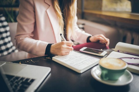 Close up caucasian woman hand on wooden table inside cafe makes notes in notebook. Subject
