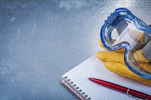 Plastic goggles leather gloves copybook pen on metallic background