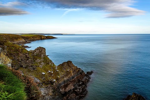 Scenic view of cliffs in Old Head of Kinsale peninsula in Ireland with green hills at sunset