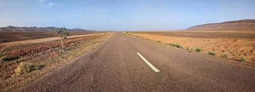 Panorama of an empty long, straight road in south Morocco, surrounded by an arid landscape