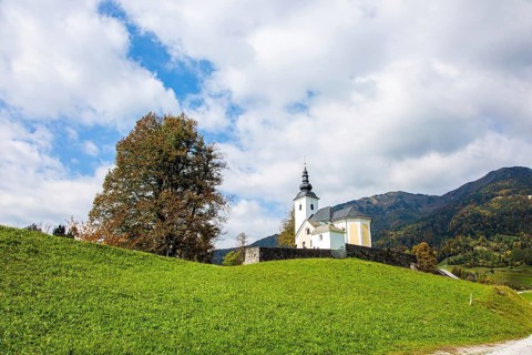White church and bell tower on a hill near the small village. Green grassy lawns in a mountain