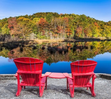 Red plastic loungers on the shore of the pond. Foliage of forests is reflected in the pond.