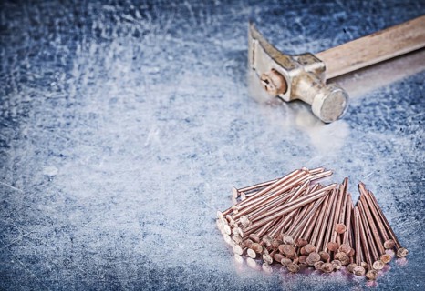 Vintage claw hammer stack of copper construction nails on metallic background