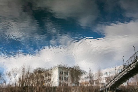 Building and part of a bridge are reflected in the river Mur, Leoben, Styria, Austria, Europe