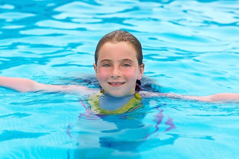 Blond kid girl swimming in the pool with sun tan red cheeks