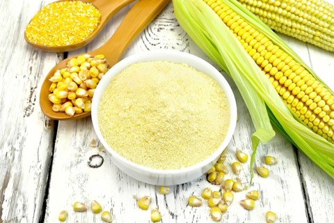 Flour corn in a bowl, groats and grain maize in the spoons, cobs on the background white wooden