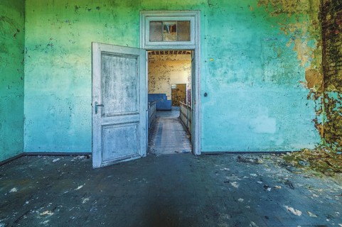 Open wooden door in a dilapidated room with peeling green wall paint, Prison H11, Lost Place,