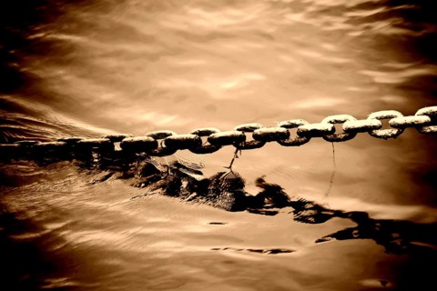 The bizarre and brute toning of an anchor chain protruding from a body of water