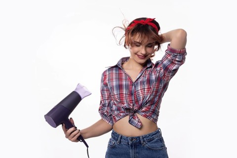 A stylish and fashionable young woman is playfully and joyfully using a hair dryer, showcasing her