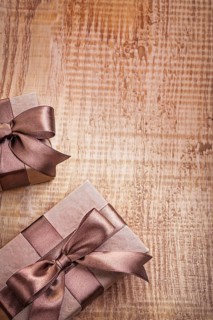 Conceptual copyspace photo two brown paper giftboxes with ribbons on vintage wooden board