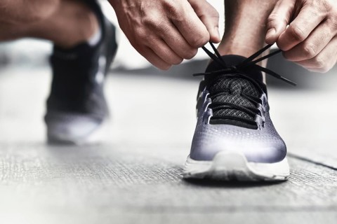 Cropped image of hands tying shoelaces on sneaker, running surface background. Hands of sportsman