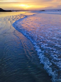 A serene beach scene with gentle waves reflecting a vivid sunset sky, creating a calm and peaceful