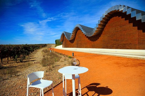 Table and chairs for tourists. Fragment of the facade. Wave-shaped winery roof. Winery - bodega