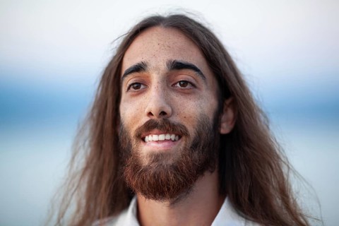A portrait of a young man with long hair, a beard and a kind smile on his gace