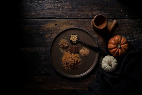 Top view of various ground handfuls of pumpkin spices on dishware and spoon at wooden plank table