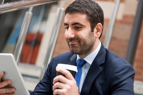 Confident businessman sitting on steps with tablet and coffee