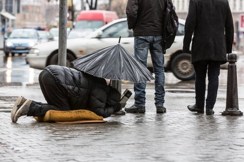 Homeless beggar is begging for money in a main street in Sofia holding an umbrella in a rainy day.