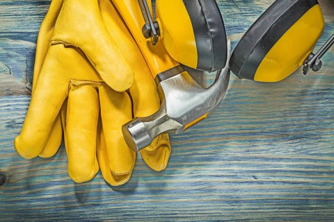 Leather yellow safety gloves ear muffs claw hammer on wooden board construction concept