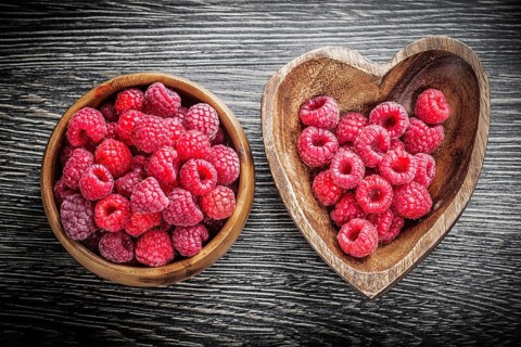 Round and heart-shaped bowls with raspberries on wooden board