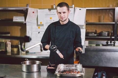 Theme cooking. A young Caucasian man in black uniform and latex gloves at a restaurant in the