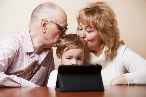 Grandparents kissing their little grandson who is busy with touchpad
