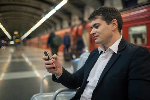 Young businessman using smartphone while waiting at the underground station. Blurred platform,